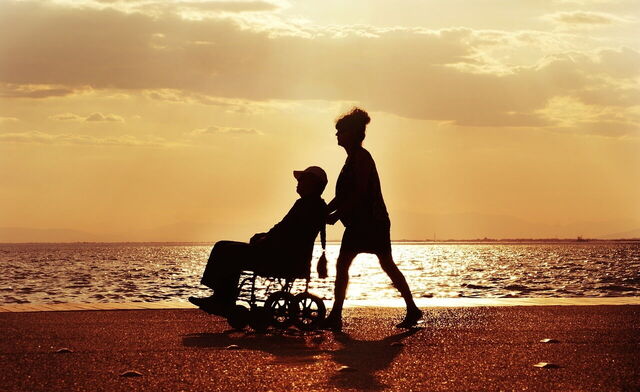 A gentleman in a wheelchair being pushed by a woman on a beach