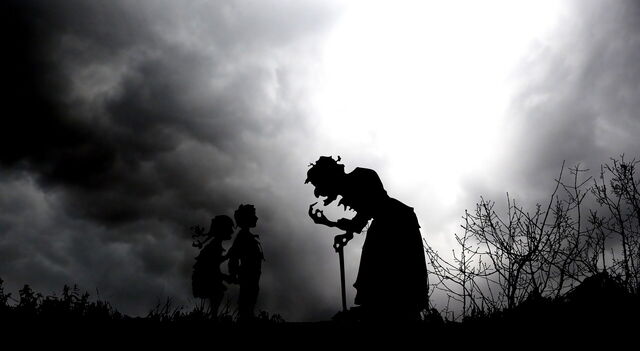 A silhouette of a witch and two kids at night